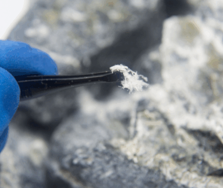 Close-up of a gloved hand holding a fibrous asbestos mineral sample above a rock surface.