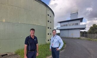 Two men standing in front of the Mt Basset 450,000 litre water reservoir and adjacent radar building in Queensland