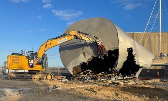 Excavator completing controlled collapse of a large steel tank