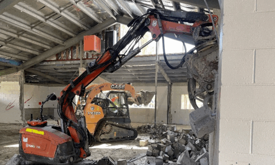 Interior of a school building mid-renovation with exposed ceilings and demolition tools in use.